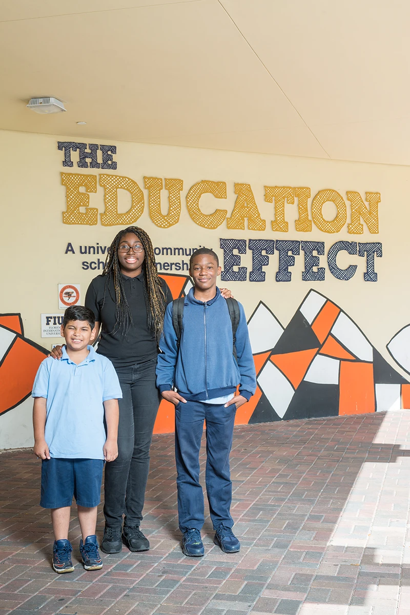 Three students standing next to the banner for the Education Effect